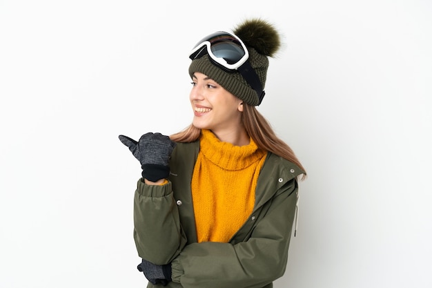 Esquiadora mulher caucasiana com óculos de snowboard isolados no branco apontando para o lado para apresentar um produto