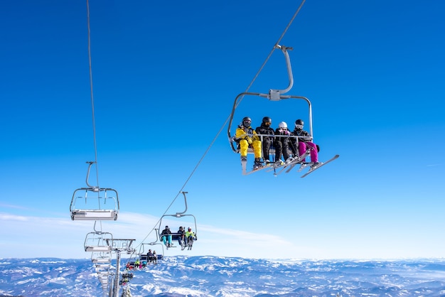 Esquiadores em um elevador de esqui em um resort de montanha com o céu e as montanhas ao fundo