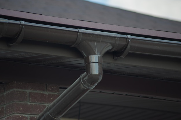 Esquina de la casa con nuevo techo de tejas de metal gris y canalón de lluvia Sistema de canalones metálicos Canalones y tubería de drenaje Exterior