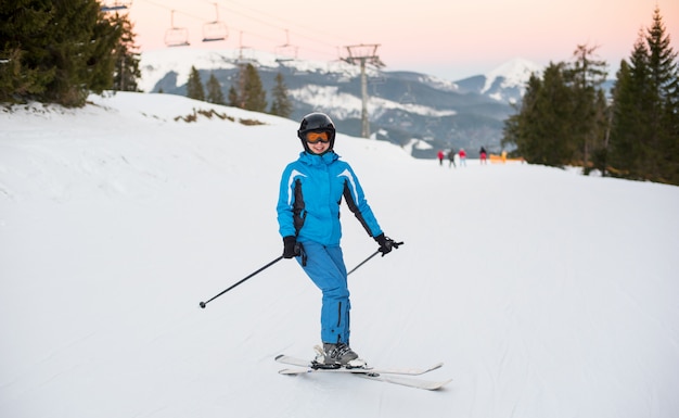 Esquis de sorriso da equitação da mulher na montanha nevado em um recurso do inverno com os elevadores de esqui no fundo.