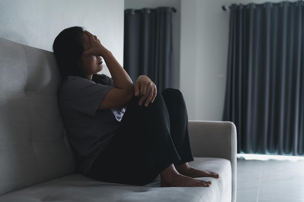 Esquizofrenia com solidão e tristeza no conceito de depressão de saúde mental Mulher deprimida sentada no sofá em casa com quarto escuro sentindo-se miserável As mulheres estão deprimidas com medo e infelizes