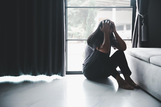 Foto esquizofrenia con soledad y tristeza en el concepto de depresión de salud mental mujer deprimida sentada contra el suelo en casa con un cuarto oscuro sintiéndose miserable las mujeres están deprimidas temerosas e infelices