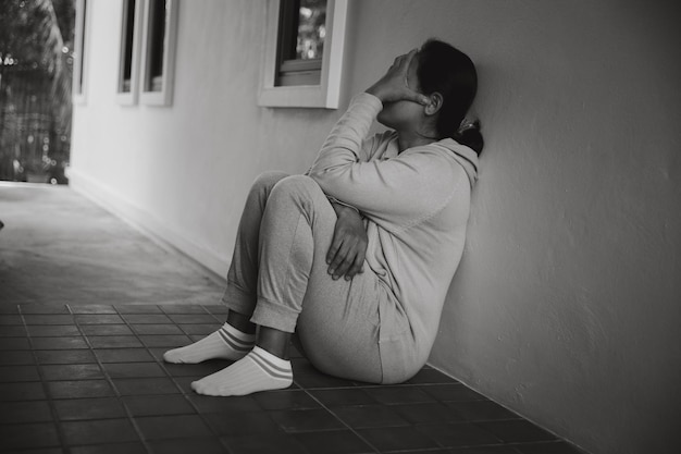 Esquizofrenia con soledad y tristeza en el concepto de depresión de salud mental Mujer deprimida sentada contra el suelo en casa con un cuarto oscuro sintiéndose miserable Las mujeres están deprimidas temerosas e infelices