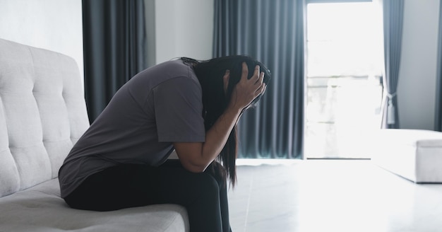 Foto esquizofrenia con soledad y tristeza en el concepto de depresión de salud mental mujer deprimida sentada en el sofá de casa con un cuarto oscuro sintiéndose miserable las mujeres están deprimidas temerosas e infelices