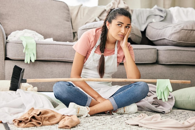 Essas tarefas podem simplesmente desaparecer Foto de uma jovem sentada parecendo sobrecarregada enquanto está sentada em uma sala de estar bagunçada em casa