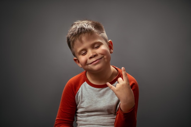 Esse garoto balança o tolo de emoções satisfeitas garotinho mostrando gesto de pedra com os olhos felizes fechados hum ...