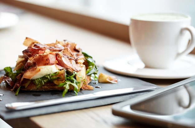 Essen, Abendessen, Haute-Küche und Essen-Konzept - Schinken-Prosciutto-Salat auf Steinplatte mit Tablet-PC und Getränk im Restaurant