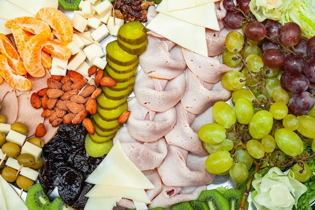 Essen auf einem Tablett Schinken Käse Pflaumen Mandeln Rosinen Weintrauben Mandarinenscheiben Oliven Scheiben Kiwi