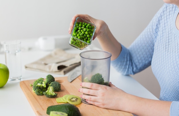 Essen, Babynahrung, gesunde Ernährung und Kochkonzept - Nahaufnahme einer Frau, die mit der Hand Erbsen zu einem Messbecher mit Brokkoli hinzufügt