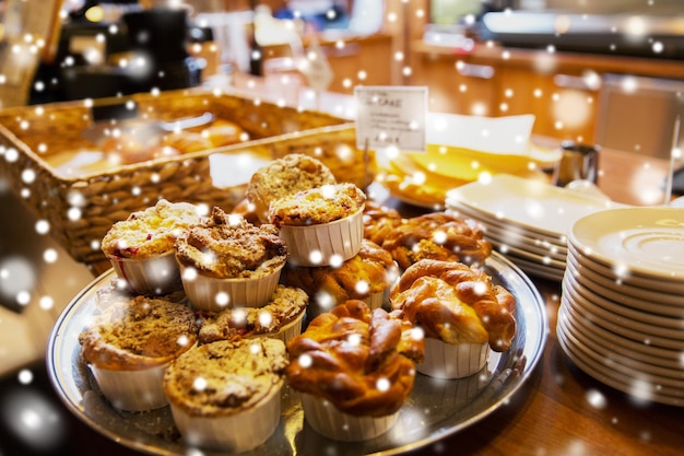 Foto essen, backen, junk-food und weihnachtskonzept - butterbrötchen oder kuchen am stand im café oder in der bäckerei über schnee