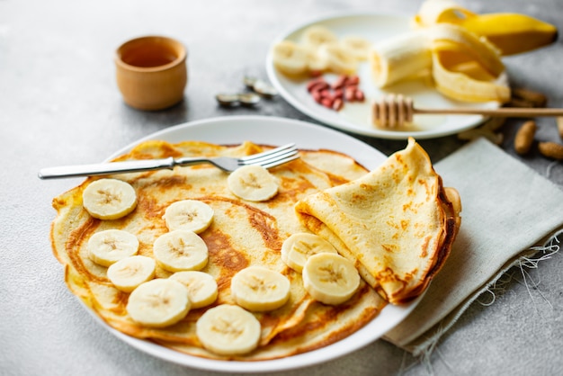 Foto essen, dessert, gebäck, pfannkuchen, kuchen. geschmackvolle schöne pfannkuchen mit banane und honig auf einem konkreten hintergrund