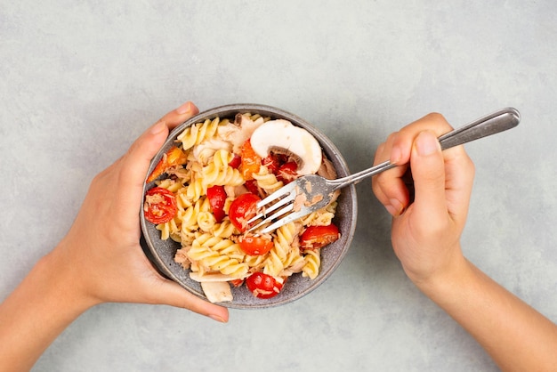 Essen eines Nudelsalats mit geschnittenen Pilzen, Tomaten, Paprikastücken, Thunfisch, gesundes Essen mit Gemüse