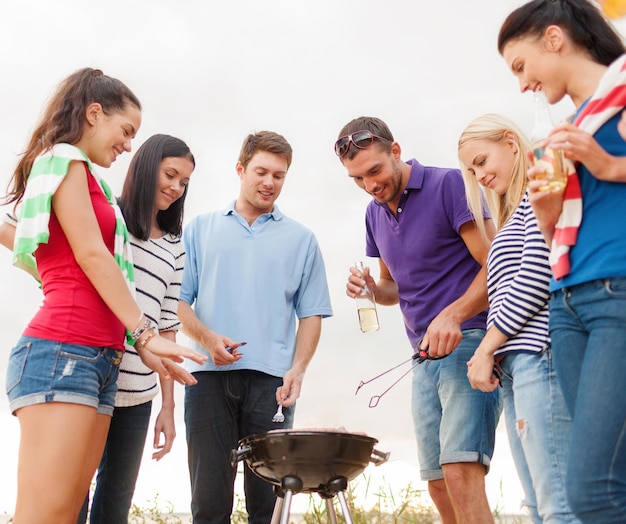 essen, essen, kochen, sommerferien und personenkonzept - gruppe von freunden, die picknick machen und am strand grillen