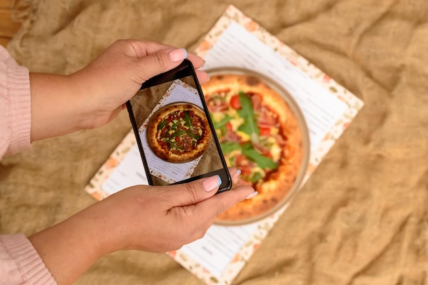 Essen fotografieren. Hände, die leckere Pizza mit Smartphone fotografieren.