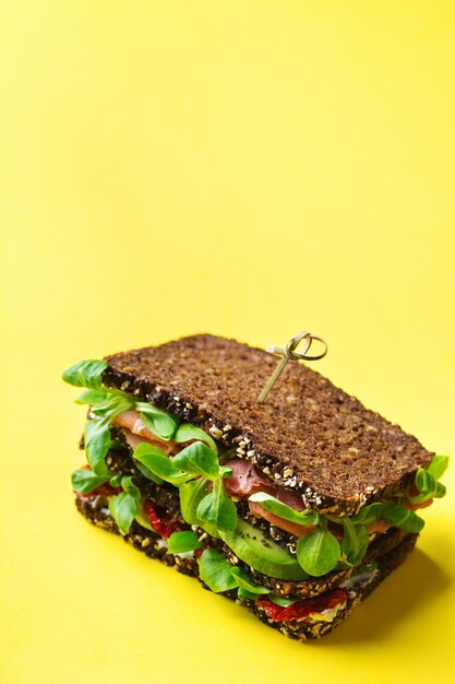 Essen, Frühstück, Morgen- und Mittagskonzept. Frisches gesundes Roggenbrot-Sandwich mit Schinken, Salat und getrockneten Tomaten auf trendigem gelbem Hintergrund. Platz kopieren