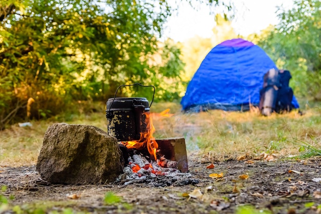 Essen in einem Wasserkocher am Lagerfeuer im Wald kochen. Zelt im Hintergrund