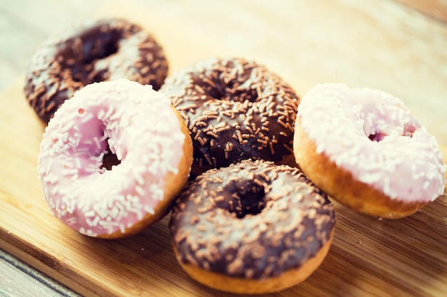 Foto essen, junk-food und esskonzept - nahaufnahme von glasierten donuts auf holzbrett