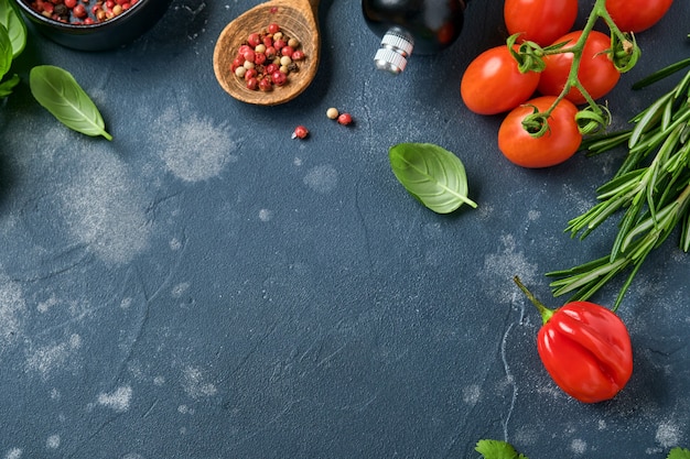 Essen kochen Hintergrund. Frischer Rosmarin, Koriander, Basilikum, Kirschtomaten, Paprika und Olivenöl, Gewürzkräuter und Gemüse am schwarzen Schiefertisch. Draufsicht der Lebensmittelzutaten.