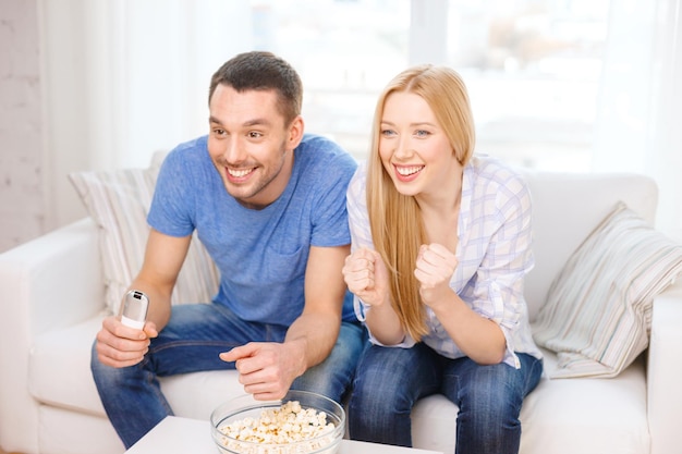 Essen, Liebe, Familie, Sport, Unterhaltung und Glückskonzept - lächelndes Paar mit jubelndem Popcorn-Sportteam zu Hause