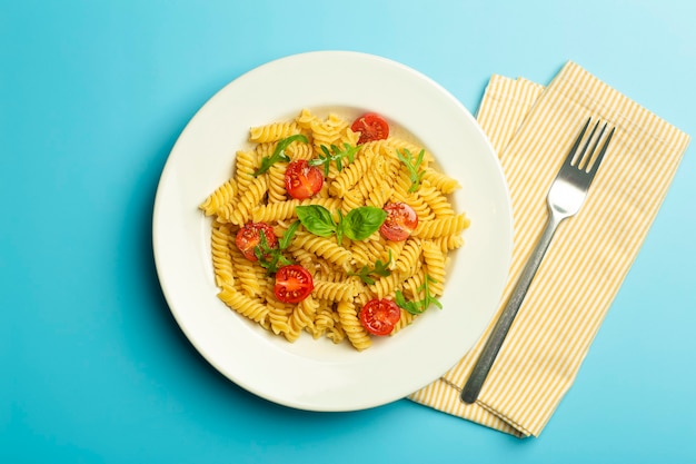 Essen Nudeln auf einem blauen Hintergrund. Italienische Fusilli-Nudeln mit Tomaten, Kräutern und Basilikum auf einem weißen Teller.