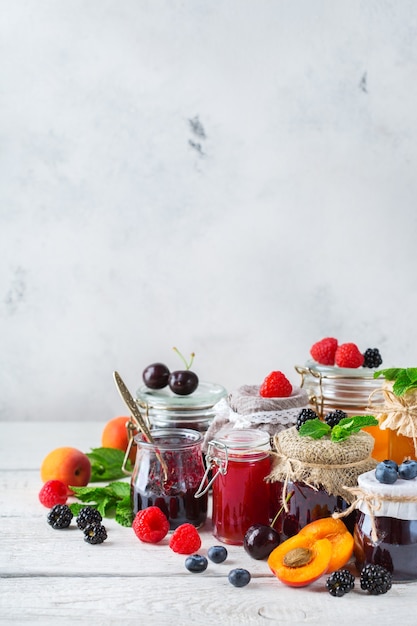 Essen und Trinken, Erntesommer-Herbst-Konzept. Auswahl an saisonalen Beeren und Fruchtmarmeladen in Gläsern auf einem Holztisch. Rustikaler Hintergrund des Raumes kopieren