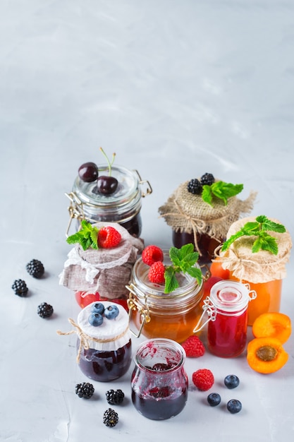 Essen und Trinken, Erntesommer-Herbst-Konzept. Auswahl an saisonalen Beeren und Fruchtmarmeladen in Gläsern auf einem Holztisch. Rustikaler Hintergrund des Raumes kopieren