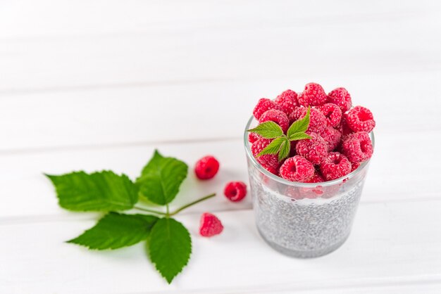 Essen und Trinken, gesunde Ernährung und Diätkonzept. Hausgemachter weißer Chia-Pudding mit frischen Beeren und grünen Blättern zum Frühstück auf einem hellen Küchentisch.