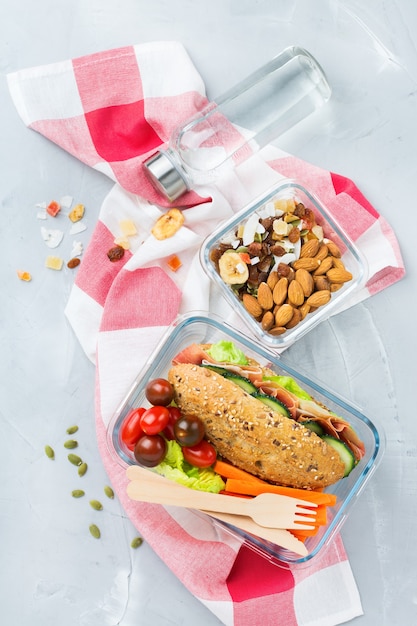 Essen und Trinken, Stillleben, Diät und Ernährung, gesunde Ernährung, Konzept zum Mitnehmen. Lunchbox mit Sandwich, Obst, Gemüse, Nussmischung und einer Flasche Wasser. Draufsicht flach legen Hintergrund