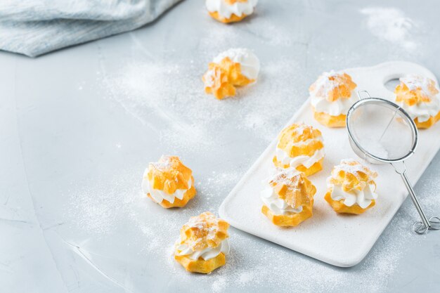 Essen und Trinken, Urlaubskonzept. Köstliche süße hausgemachte Profiteroles mit Sahne auf einem modernen Küchentisch. Raumhintergrund kopieren