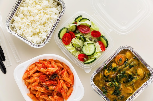 Essen zum Mitnehmen in Einwegbehältern Reis Gemüse Curry italienische Pasta mit Tomatensauce und frischem gesundem Salat