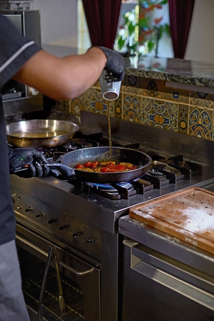 Essenskonzept Der Koch brät in einer Pfanne die Tomaten und Austern und bereitet das Gericht in der Küche zu