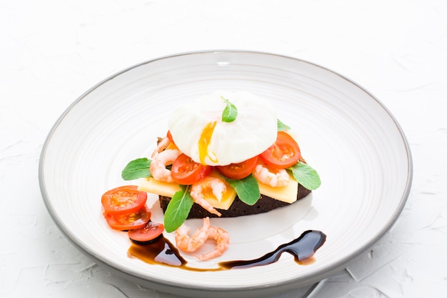 Essfertiges Sandwich auf Roggenbrot mit poschiertem Ei, Tomate, Garnele und Rucola auf einer Platte