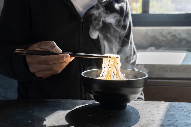 Essstäbchen zu leckeren Nudeln mit Dampf und Rauch in Schüssel auf Holzhintergrund, selektiver Fokus., asiatische Mahlzeit auf einem Tisch, Junk-Food-Konzept