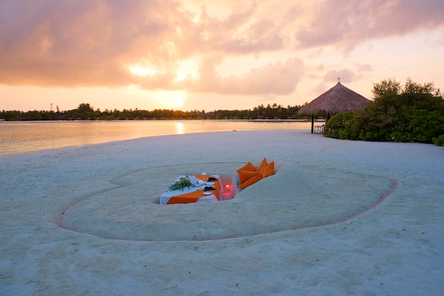 Esstisch im Sand in der Nähe des Ozeans Graben Sie den Sand, um den Esstisch bei Sonnenuntergang zu machen