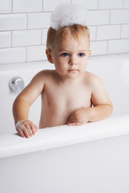 Se está bañando antes de acostarse Un adorable bebé de pie en la bañera