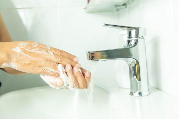 Esta é uma foto de uma mão de mulher Lavando as mãos com sabão branco espumante em uma pia branca no banheiro