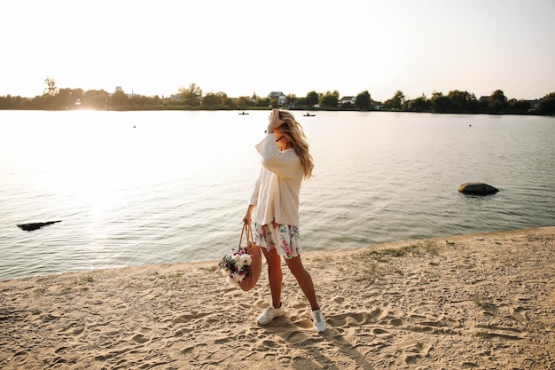 Esta foto mostra uma jovem loira andando na praia em um vestido e suéter com flores em um dia ensolarado