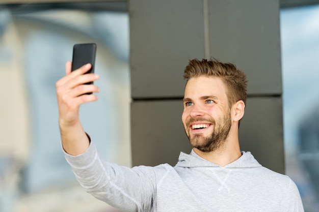 Estaba esperando tu llamada Hombre barba con fondo urbano de teléfono inteligente Concepto de comunicación Chico alegre videoconferencia teléfono inteligente Hombre con barba feliz cara sonriente videollamada