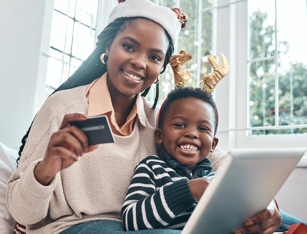 Estábamos haciendo algunas compras navideñas desde casa Fotografía de una mujer sosteniendo su tarjeta de crédito y sosteniendo una tableta digital mientras estaba sentada con su hijo durante la época navideña