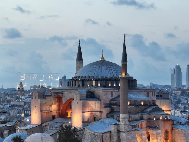 Estabelecimento de uma foto aérea de uma Grande Mesquita de Hagia Sophia com a Ponte do Bósforo e o horizonte da cidade com uma bandeira no fundo em Fatih, Istambul, Turquia, ao pôr do sol
