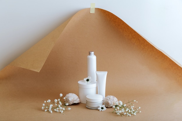 Establecer productos cosméticos de belleza natural para el cuidado de la piel con conchas de mar de flores sobre fondo marrón beige. Productos femeninos cosméticos de la loción del tubo de crema del kit blanco para la maqueta cosmética del cuidado de la piel del tratamiento del cuerpo.