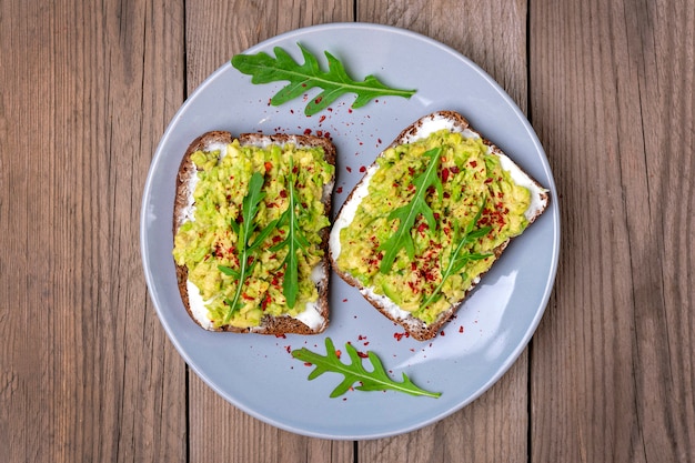 Establecer sándwiches para el desayuno - rebanada de pan integral oscuro, guacamole sobre mesa de madera