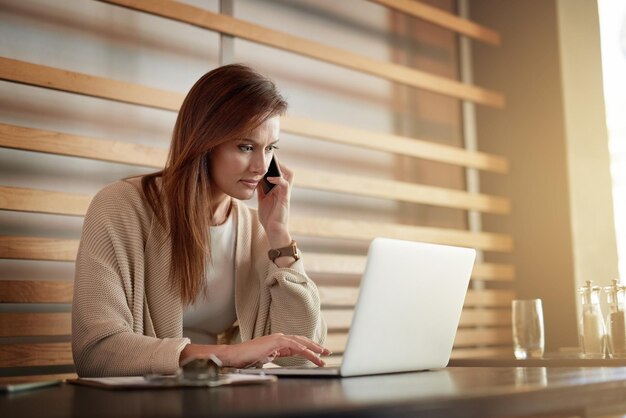 Estableciendo oportunidades de negocios en el café Foto de una mujer joven hablando por un teléfono celular mientras trabaja en su computadora portátil en un café