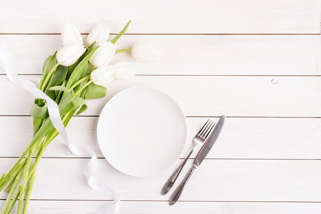 Establecimiento de mesa festiva en plato blanco blanco y tulipanes vista superior en fondo de madera