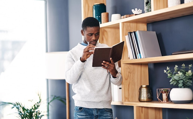 Establezca metas y llévelas a cabo Captura de un joven empresario leyendo un cuaderno en una oficina moderna