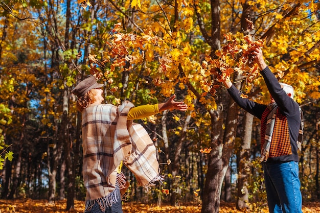 Foto estação de outono casal jogando folhas na floresta de outono família idosa se divertindo ao ar livre jogando jogos