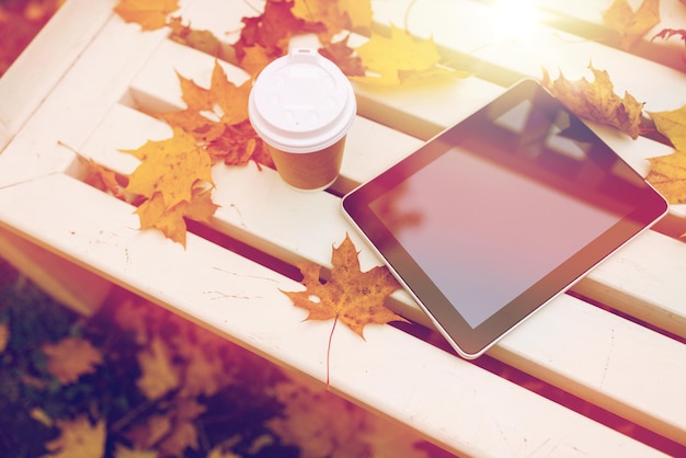 Foto estação, tecnologia e conceito de publicidade - computador tablet e xícara de papel de café no banco no parque de outono