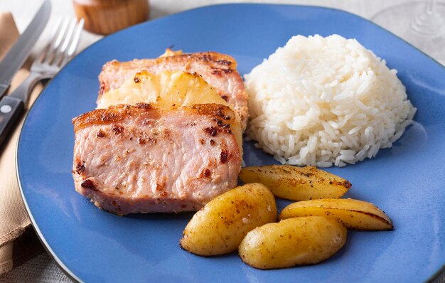 Foto estacas de porco com arroz de abacaxi e batatas sobre prato azul