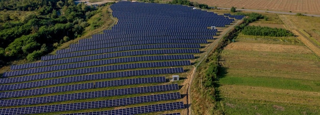 Estación de energía solar en campo verde en día soleado Vista aérea Los paneles solares se encuentran en una fila en el campo para la producción de energía Drone sobrevuela la granja solar Energía verde renovable Fuentes de energía alternativas