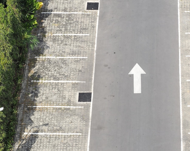 Estacionamento ao ar livre e linha branca de concreto e seta branca e árvore.